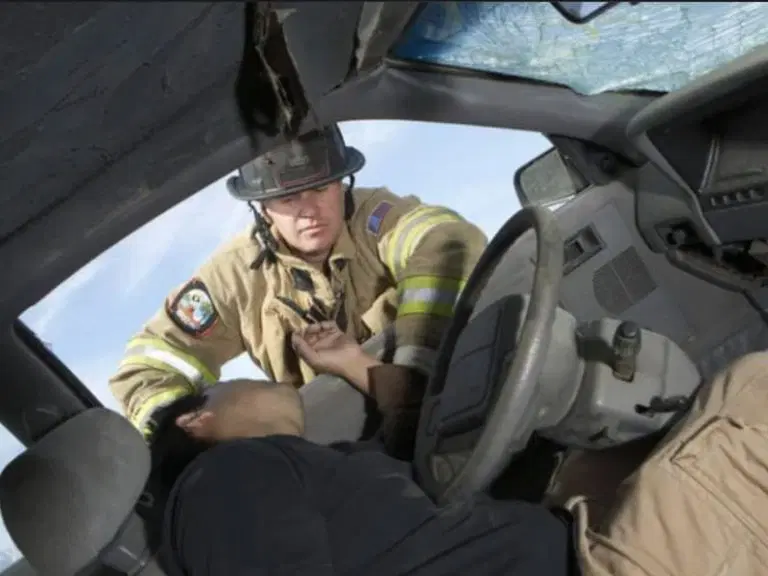 A firefighter assists an injured person inside a damaged car with a shattered windshield after an accident.