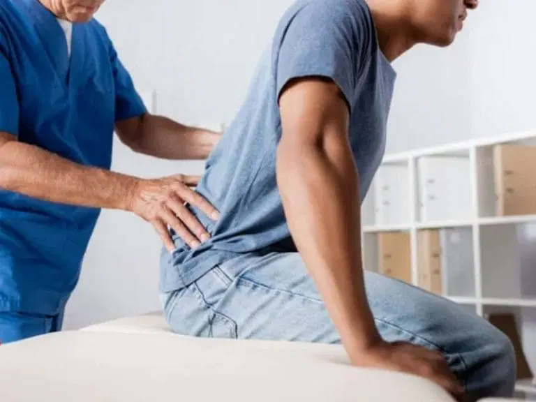 A healthcare professional examines a man's lower back as the man sits on an examination table.