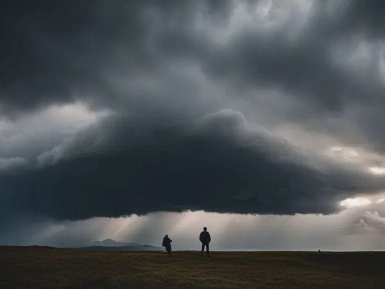 Two people stand on open ground beneath a large, dark storm cloud with distant sunlight breaking through the clouds in the background.