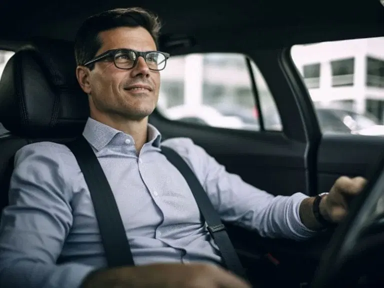 A man wearing glasses and a button-up shirt with suspenders sits in the driver's seat of a car, looking ahead and smiling slightly, embodying confidence and calm—perfect for practicing Safe Driving Tips.