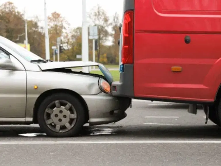 A silver car with front-end damage has collided with the rear of a parked red van on a roadway, highlighting the importance of Safe Driving Tips to help prevent such accidents.