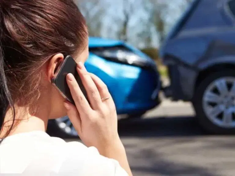 A woman is making a phone call while standing near two cars that have been involved in a rear-end collision.