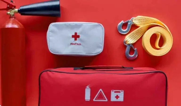 A fire extinguisher, a first aid kit, a red emergency bag, and two yellow tow straps with metal hooks arranged on a red background.