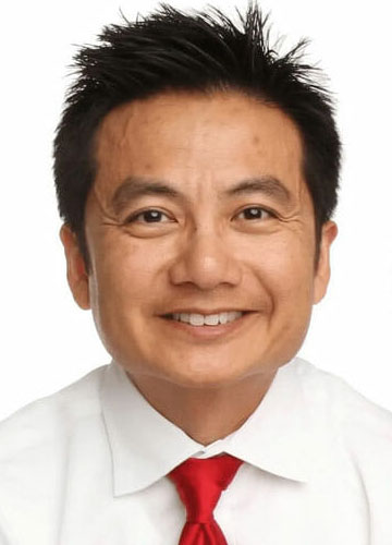 A man with short black hair, wearing a white shirt and red tie, smiles at the camera against a white background—perfect for an Accident Doctor in Phoenix.