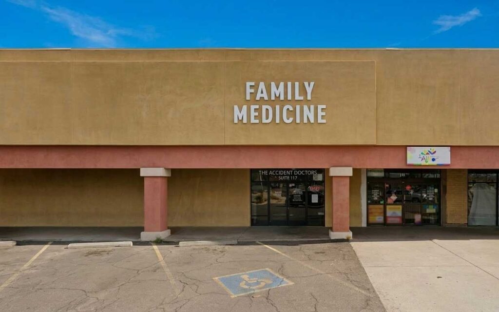 A tan building with a large "FAMILY MEDICINE" sign above a clinic entrance. A handicapped parking space is in front of the building.