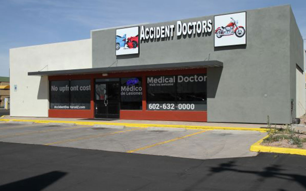 Single-story medical clinic labeled "Accident Doctors" with a parking lot in front and contact information displayed on the windows and sign.