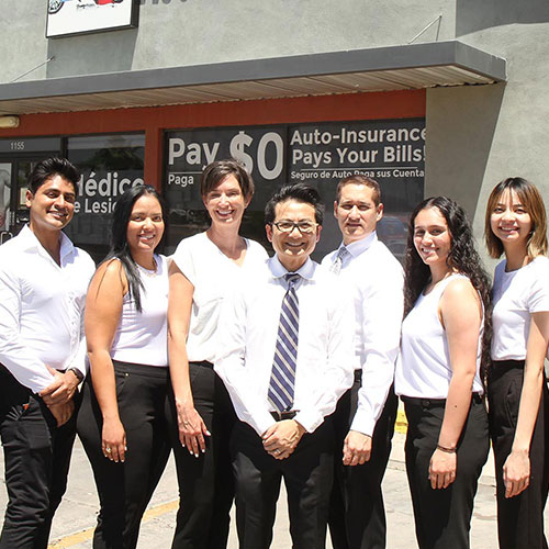 Seven people stand in front of an auto insurance office, posing for a group photo. They are dressed in business casual attire and smiling at the camera.