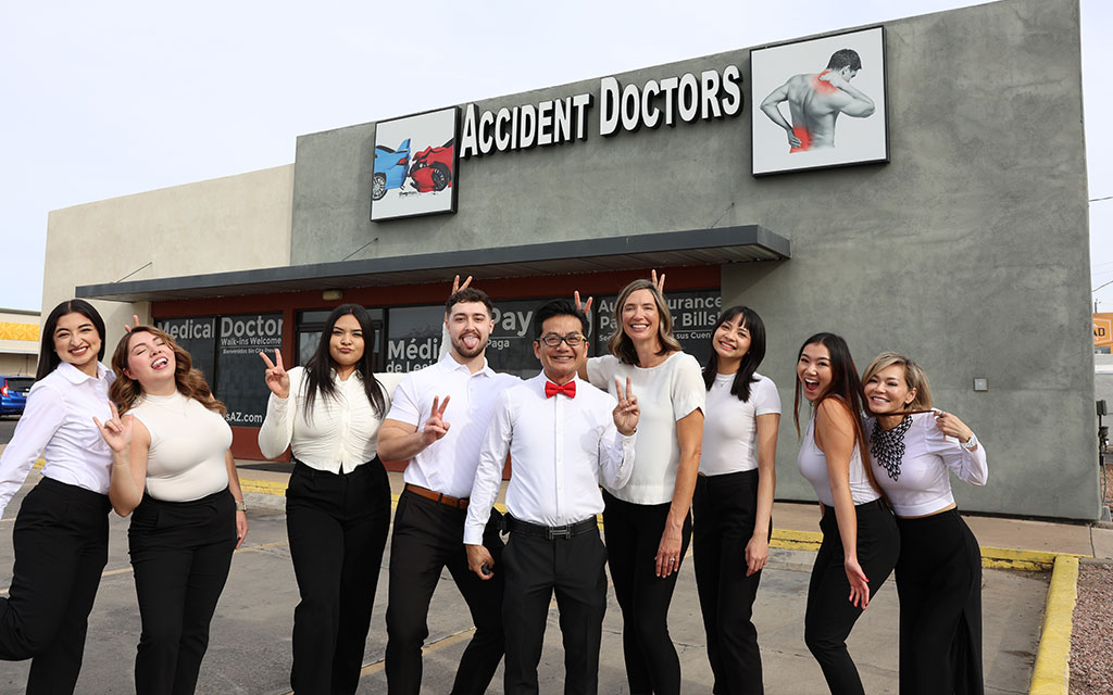 A group of nine people in coordinated black and white outfits pose and smile in front of a building with a sign that reads "Accident Doctors.